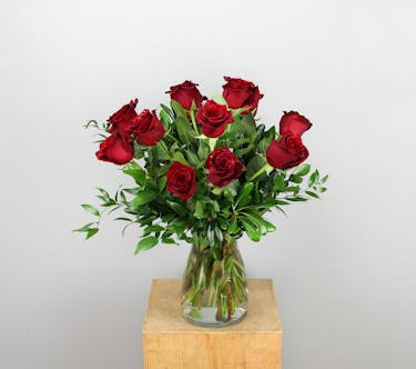 A stunning floral arrangement featuring 12 vibrant red Explorer roses elegantly arranged in a sleek clear glass vase.