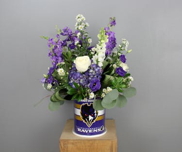 A festive purple and white Baltimore Ravens arrangement designed in a reusable tin container.